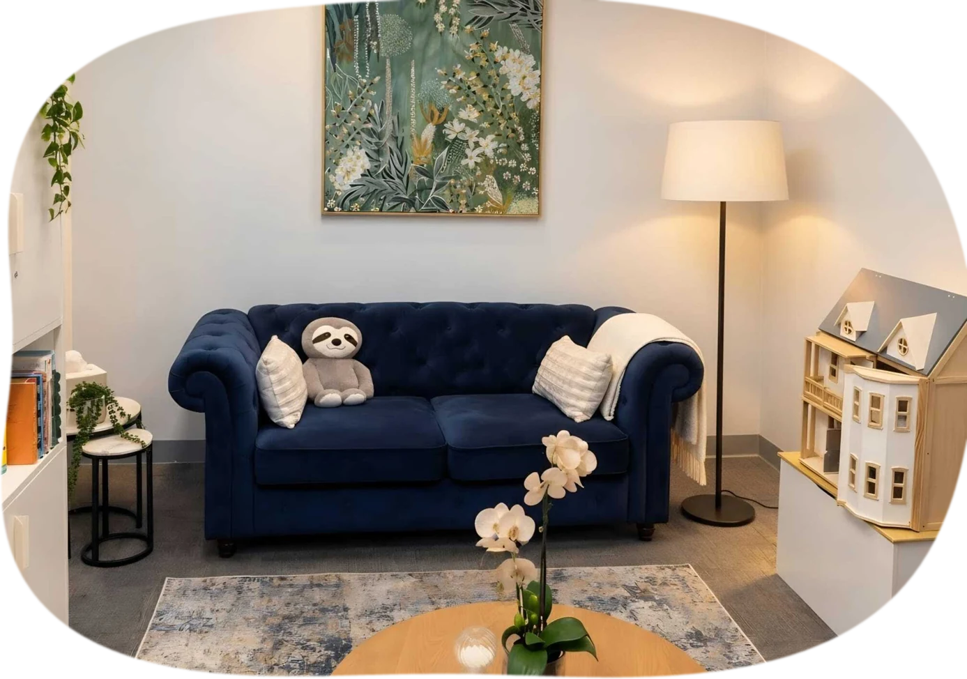 A calm consulting room at the Liverpool clinic with a navy sofa, soft lamp light, plants and a toy dolls house