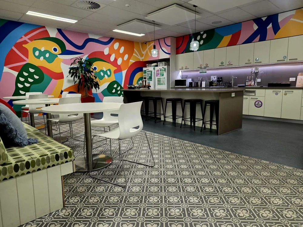 Bright kitchen and lounge area with a colourful bird mural, round tables and a long breakfast bar