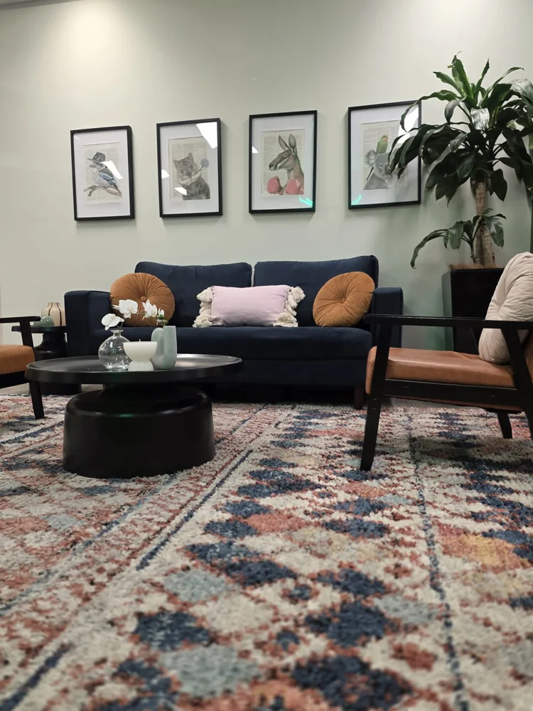 Lounge with a navy sofa, tan armchairs, a colourful rug and framed Australian animal prints